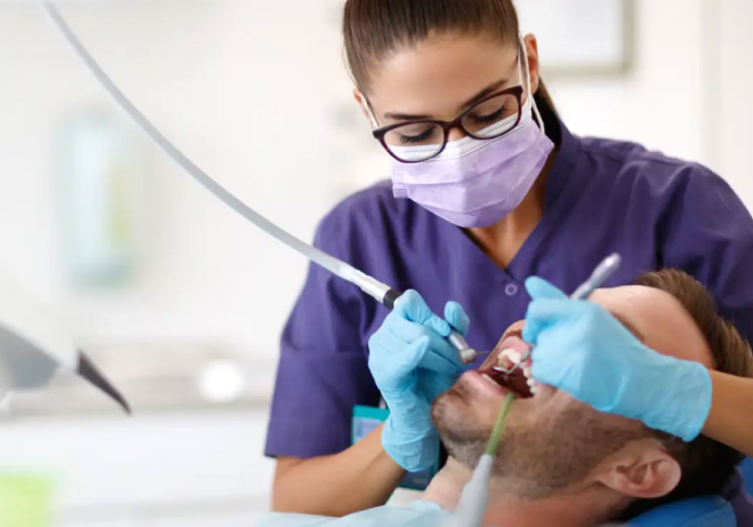Dentist wearing gloves and mask examines a patient's mouth in a dental clinic.