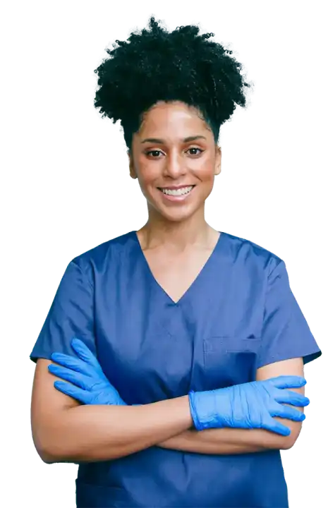 Person in blue scrubs and blue gloves stands with arms crossed, smiling at the camera.